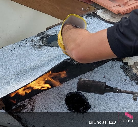 אדם משתמש במבער לאיטום גג עם יריעות ביטומניות